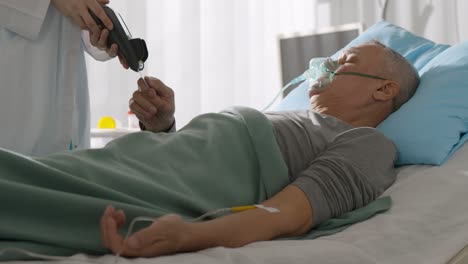 doctor holding payment terminal for aged patient lying in hospital bed and paying with credit card