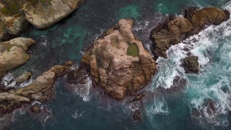 Drone-shot-of-rocks-and-waves-then-panning-up-to-reveal-the-Central-California-Coast-and-California-Highway-One