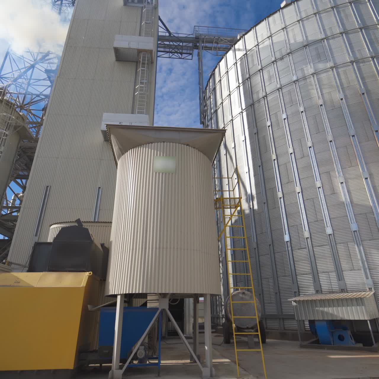Grain elevators under blue sky. Huge metal grain storage tanks. Silver containers. Close-up