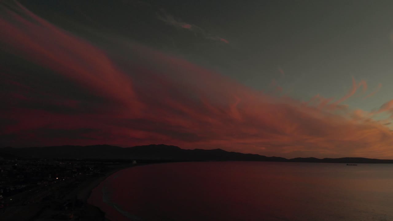 Luftaufnahme mit Drohne eines ruhigen Meeres mit dramatischem rotem Sonnenuntergangshimmel und ferner Küstenlinie, friedliche Meereslandschaft mit glatter Wasseroberfläche und sanftem Abendlicht, das eine ruhige Atmosphäre schafft