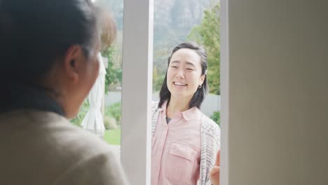 Happy-asian-mother-embracing-adult-daughter-arriving-at-backdoor