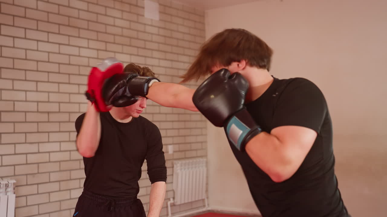 MMA fighters practice sparring inside gym, one athlete wearing black gloves defending while opponent with red pads prepares attack, showing strength, skill, intensity, movement, and discipline in martial arts