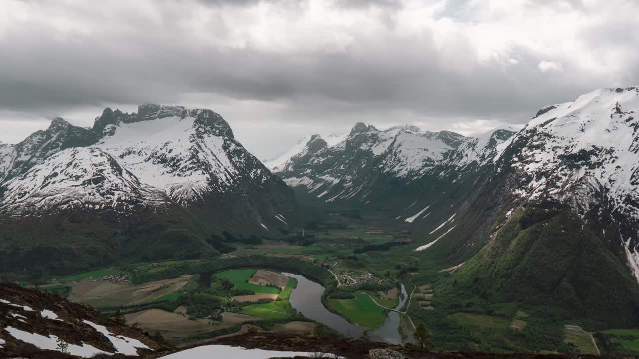 lapso de tiempo de asombrosa vista panorámica de un pequeño pueblo en un valle, nubes pasando sobre cimas de montañas nevadas