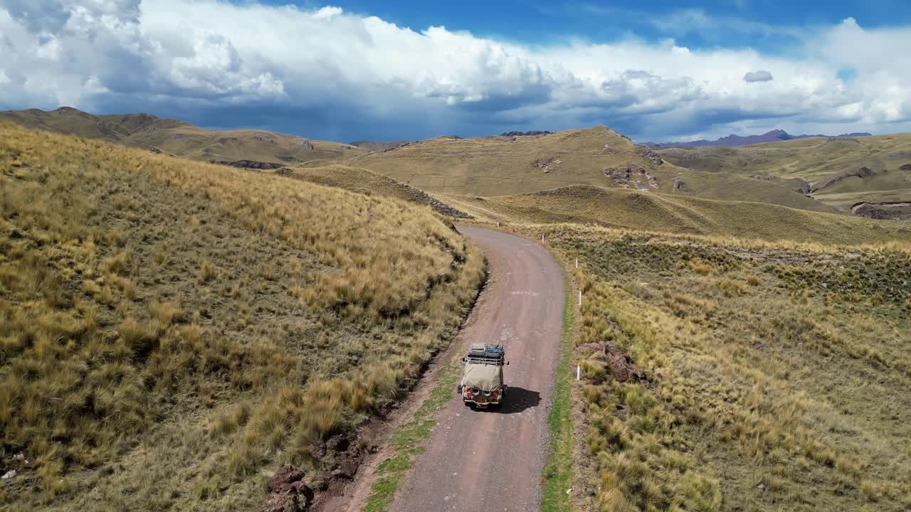 Drone footage of a yellow tuk tuk gliding through a field of soft grass in the highlands, surrounded by natural beauty and open space