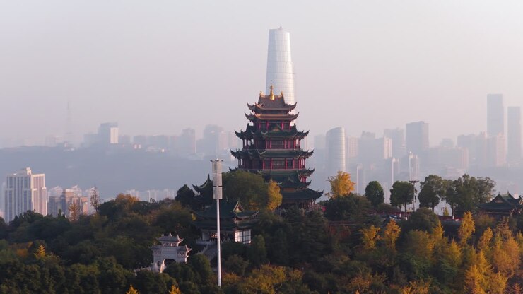 Vue au coucher du soleil du pavillon Hongen, situé sur une colline avec un feuillage d'automne, devant les gratte-ciel embrumés de Chongqing en Chine. Large plan aérien.