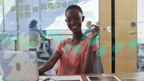 Animation-of-graph,-map,-changing-numbers-over-smiling-african-american-woman-sitting-in-office