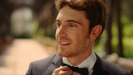 Dreamy-man-getting-better-bow-tie-in-park.-Guy-waiting-for-bride-outdoors