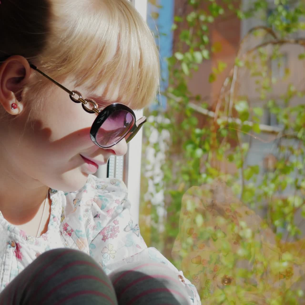 una niña de 6 años con gafas de sol mira por la ventana