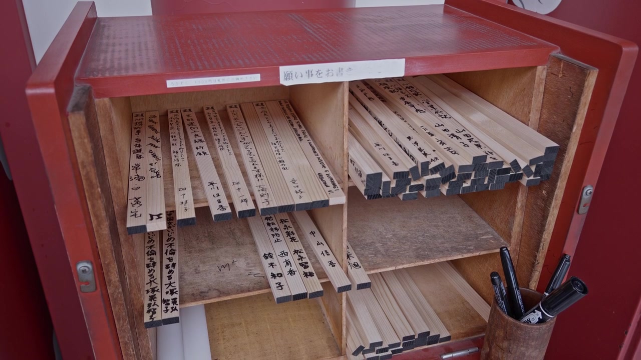 Rows of hand-inscribed wooden sticks rest in a weathered red temple cabinet, reflecting traditional Japanese religious customs and craftsmanship
