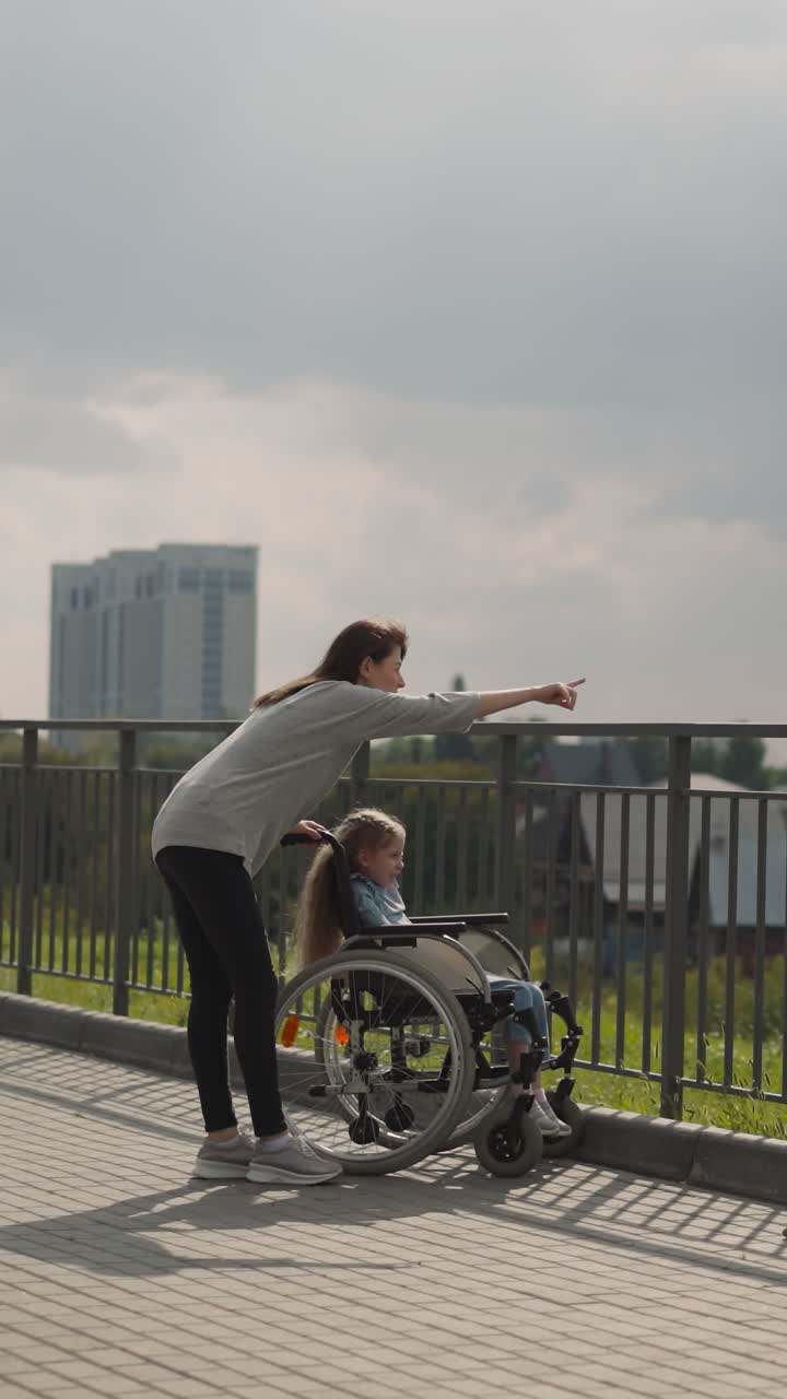 una mujer muestra la arquitectura de la ciudad a una niña sentada en silla de ruedas. madre e hija con parálisis cerebral disfrutan de un viaje familiar en un soleado día de primavera