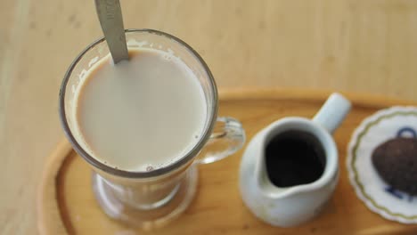 person stirring a cup of coffee or tea with milk and a small chocolate dessert on the side