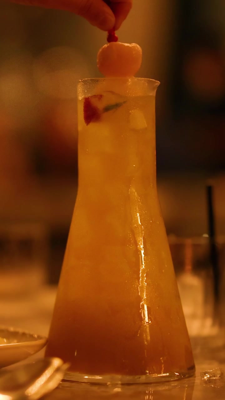 Un barista aggiunge una guarnizione di litchi a un cocktail in un ambiente da bar poco illuminato.
