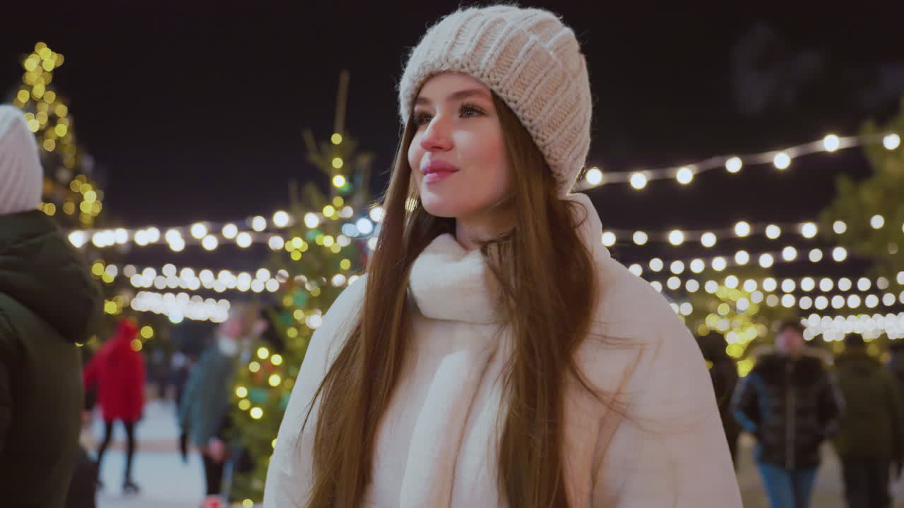Woman in cozy winter outfit strolling outdoors at night, surrounded by twinkling festive lights, Christmas decorations, and people in the background