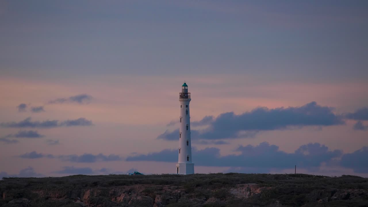 ver un lapso de tiempo del faro al atardecer en aruba, faro que ilumina el paisaje costero del caribe