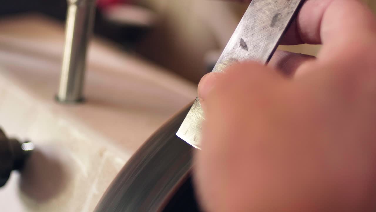 Female carpenter sharpening the metal blade of a woodworking tool on a rotating stone wheel. Slow motion close up