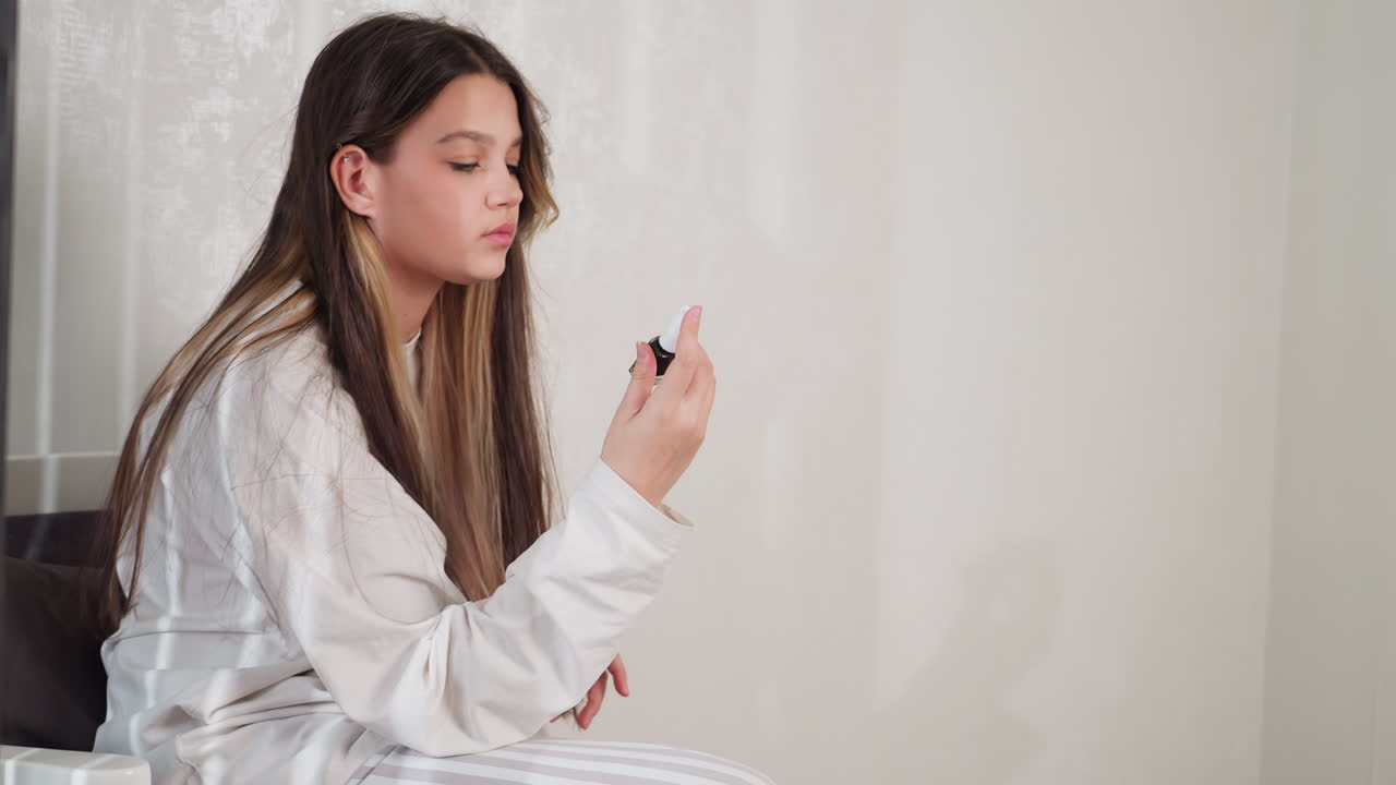 Young girl sits on chair in cozy room, lifts black nail polish bottle from side table then places it back, long hair loose, oversized light top, soft daylight mood, relaxed morning beauty moment