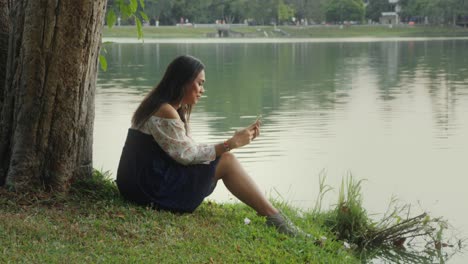 Woman using phone by lake in park