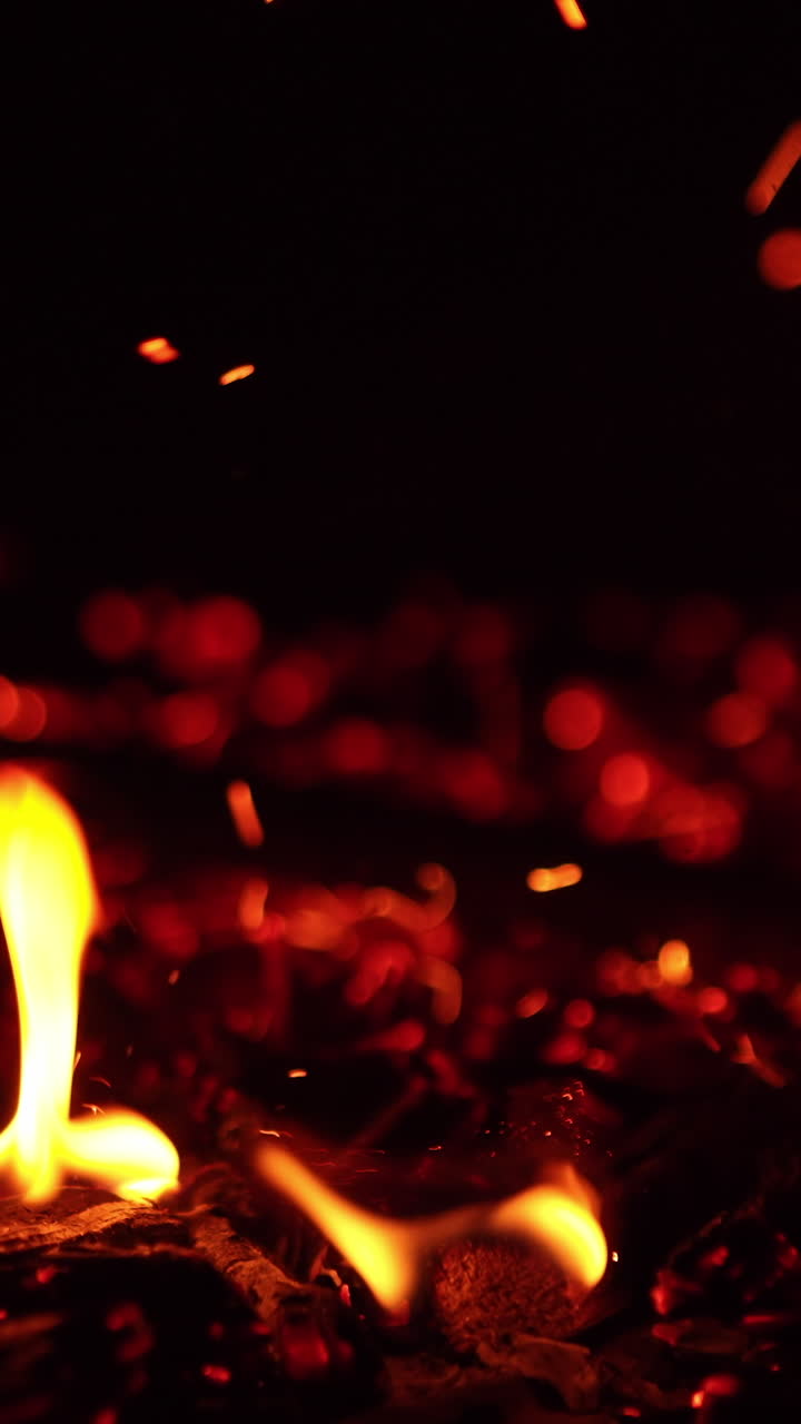 Tapping by the hot smoldering embers. Bright sparks fly up and little flames appear. Close up. Vertical video