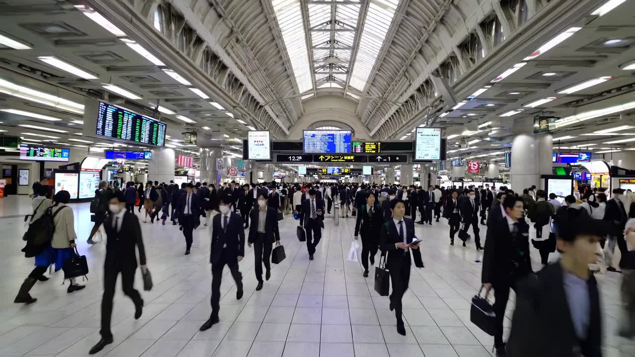 Wide-angle shot of a bustling train station interior, capturing a sea of commuters in motion