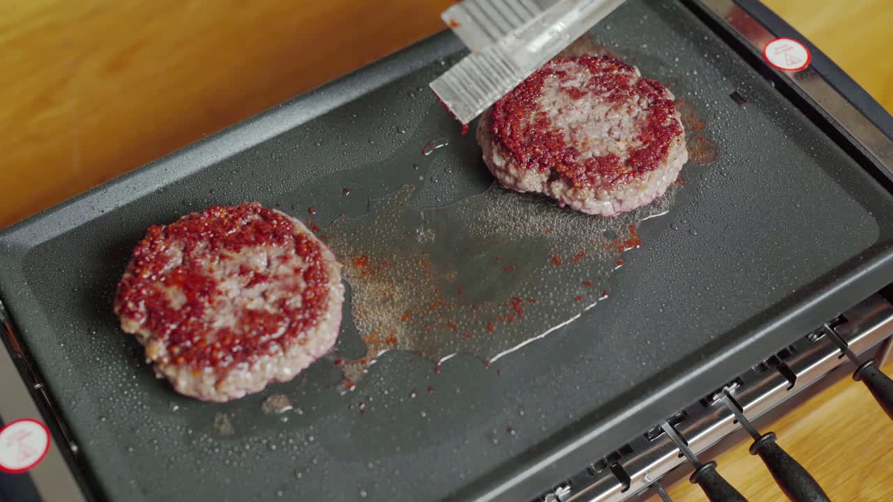 Juicy minced meat burgers turned over on electric plancha grill. Static closeup