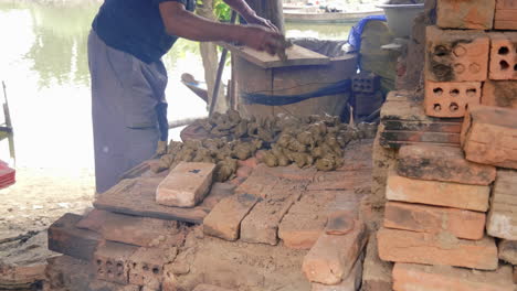 Southeast-asia-potter-places-clay-figurines-onto-earthen-kiln-by-riverside,-Than-Ha-Hoi-An-Vietnam