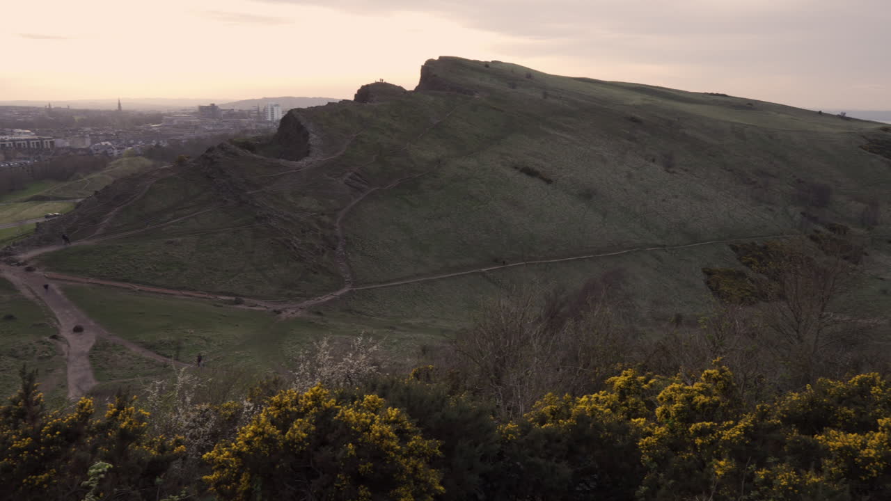 panorámica del paisaje urbano de edimburgo desde la montaña del asiento de arturs durante la puesta de sol con colores maravillosos y luz de la hora dorada con coches y personas que pasan por abajo