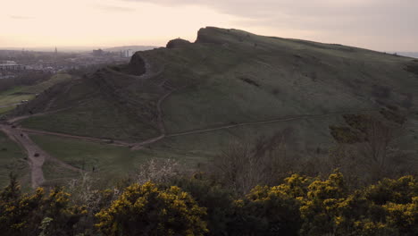 panning shot of edinburgh cityscape from the arturs seat mountain during sunset with wonderful colors and golden hour light with cars and people passing by down below