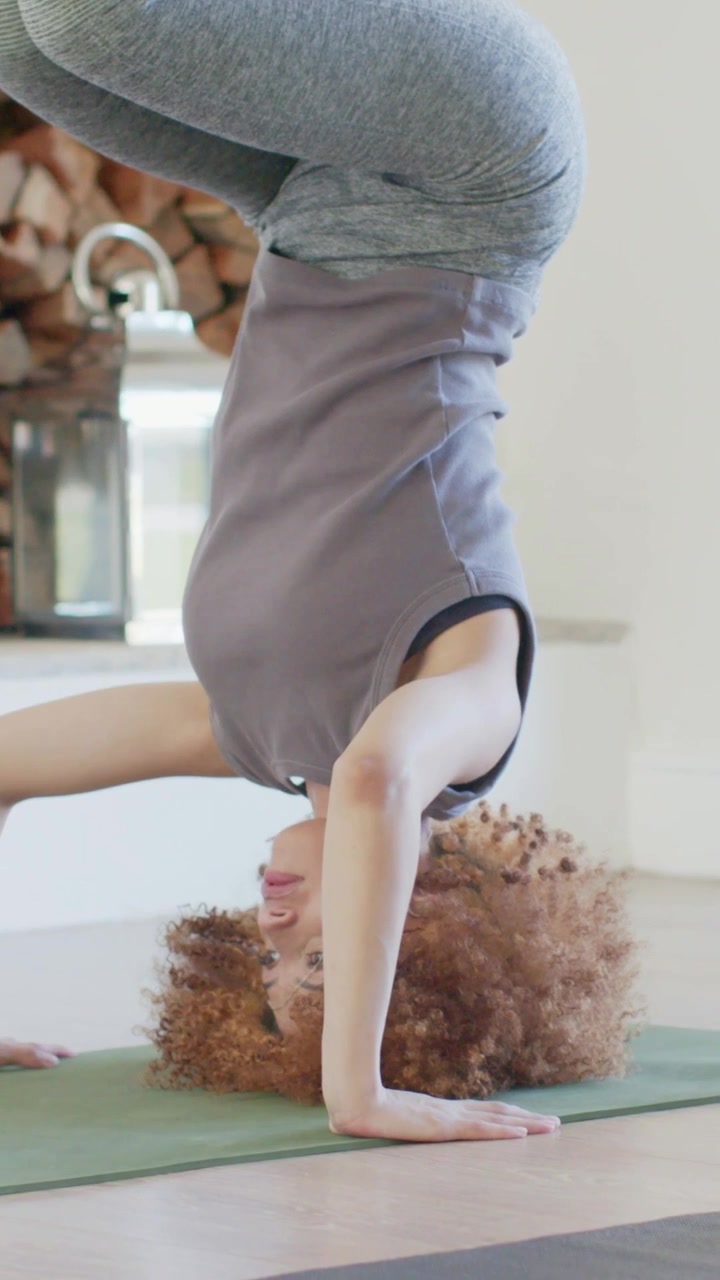 Vertical video: Placing head and hands, yogi in tank rising into headstand on home mat for balance