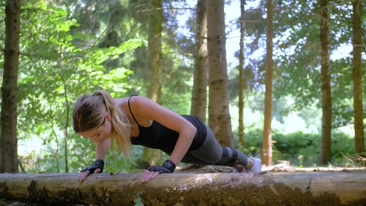 Blonde, fit woman exercising in a park by doing push-ups with her hands on a fallen tree