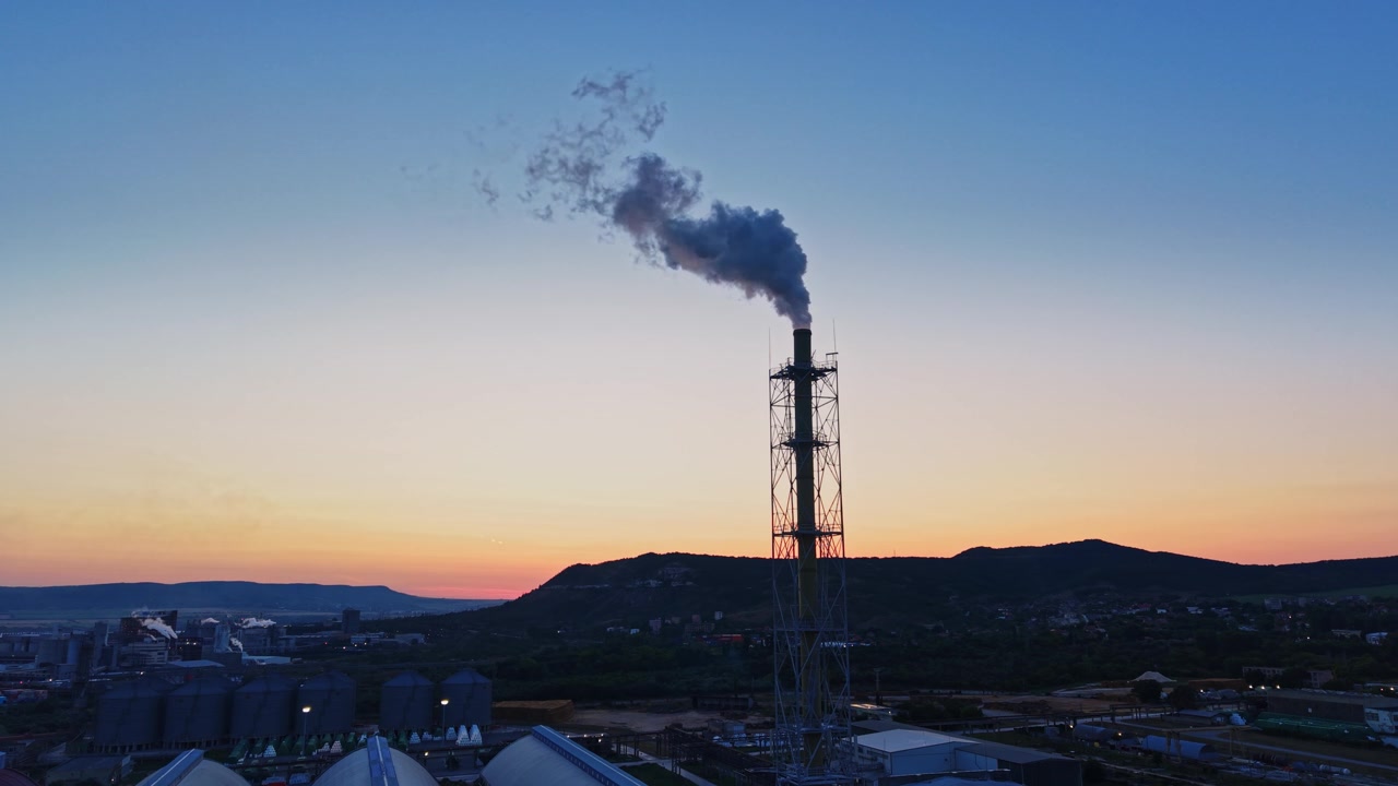 Fumo che sale da un camino al tramonto vicino a un'area industriale