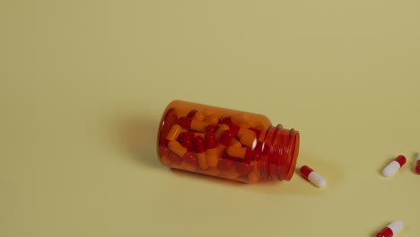 slow motion high-angle medium shot of a bottle of pills as it slides from screen left into the middle, losing its lid and spilling pills as it goes