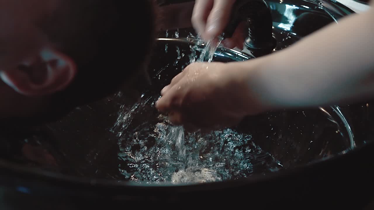 Ung mand får vasket sit hår i en frisørsalon, et nærbillede i slow motion.