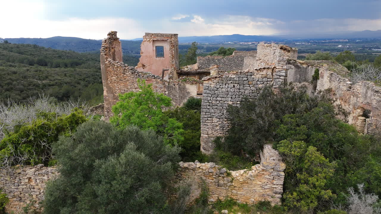 Detailed aerial view of old stone ruins surrounded by greenery, with dramatic storm clouds and distant mountains in the background