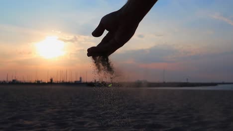 mano dejando caer un poco de arena con la puesta de sol en el fondo en la playa