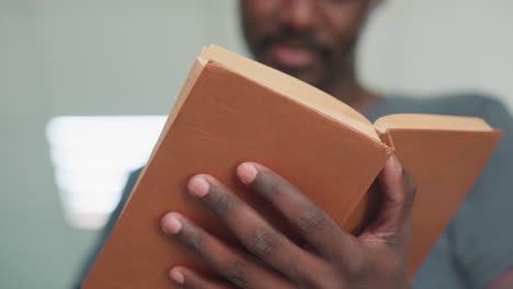 Close up of student flipping through worn brown hardcover in library, focus on hands holding book with soft blur on background and bright light behind, creating warm academic atmosphere