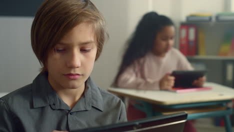 Un-Colegial-Sonriente-Sentado-En-Un-Escritorio-Con-Una-Tableta-Digital-En-La-Escuela-Primaria