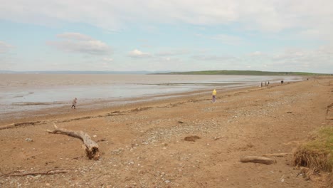 A-wide-shot-of-Sand-Bay-Beach,-showing-a-few-people-walking-along-the-shore-during-low-tide