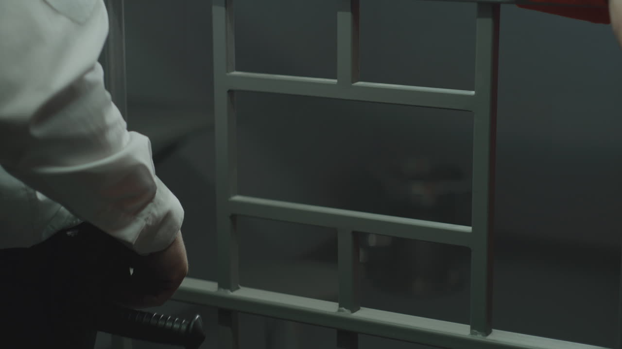 primer plano del carcelero dando el teléfono al criminal a través de barras de metal