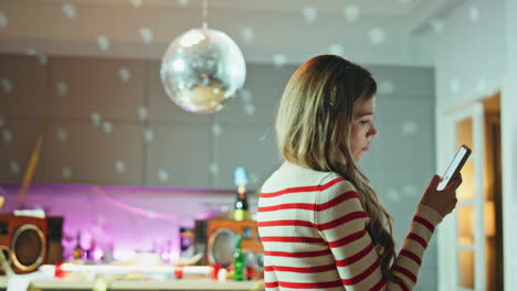 sad party girl scrolling smartphone under disco ball close up. woman reading