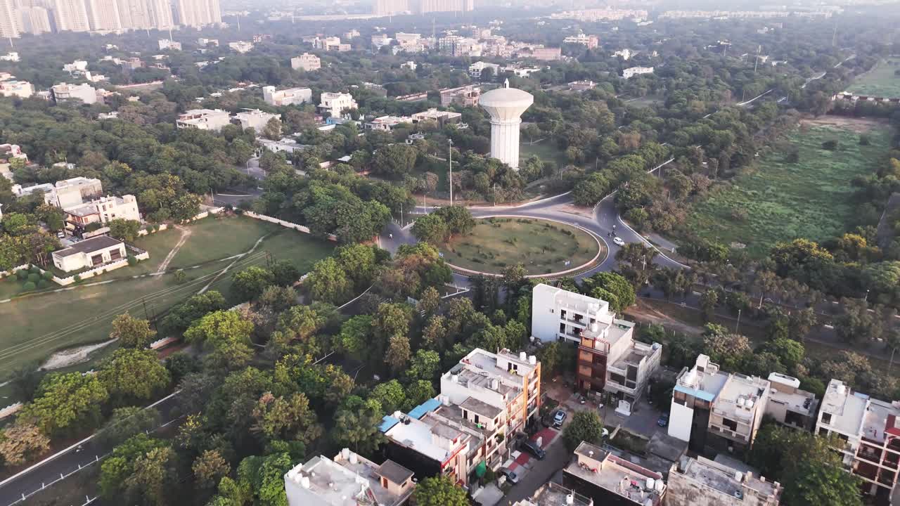 Clip di un drone che riprende un importante incrocio a Greater Noida, caratterizzato da una strada circolare, traffico leggero e vegetazione circostante, che riflettono la disposizione organizzata e la pianificazione moderna della città.