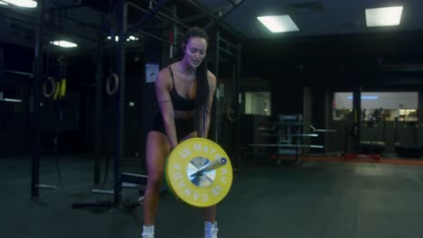 medium pull out shot of a fit girl in a gym using a landmine deadlift to work on her biceps