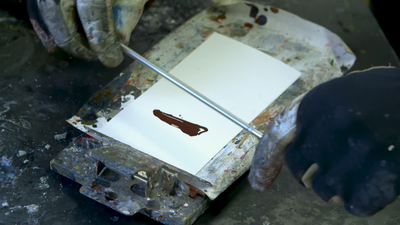 Close shot of red paint being applied to a small white paper, then smeared across the paper