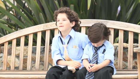 a pair of boys in formal dress sit on a wooden bench