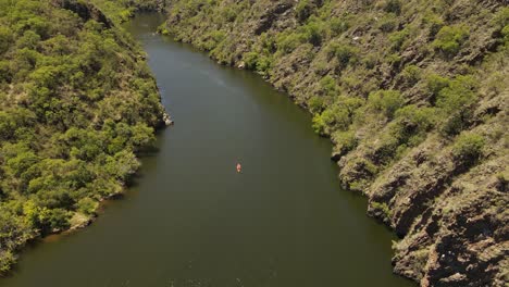 toma aérea descendente de arriba hacia abajo de un kayak naranja remando hacia abajo por el río rodeado de naturaleza pura de argentina - hermoso día soleado en sudamérica