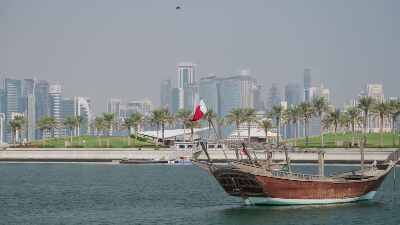 Båt med Qatar-flagg som vaier i Doha by marina og skyskraper-silhuett