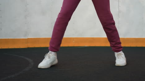 leg view of urban woman jumping around round sports court wearing white sneakers and purple joggers attire under clear sky with concrete wall and fence background vibrant movement focus on feet
