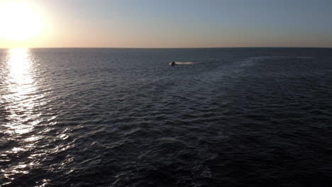 a woman on a jet ski speeds past the camera on an open ocean during sunset