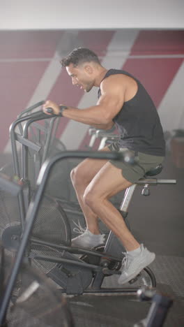 vertical video: exercising on stationary bike, man working out in gym, focusing on fitness