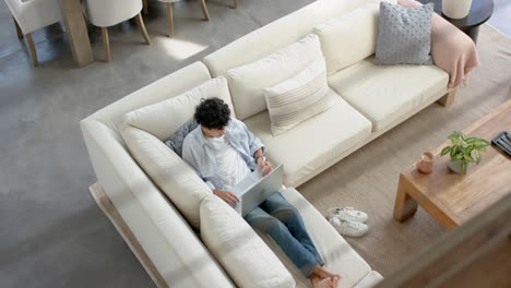 relaxing on sofa, teenage boy using laptop for work in cozy living room