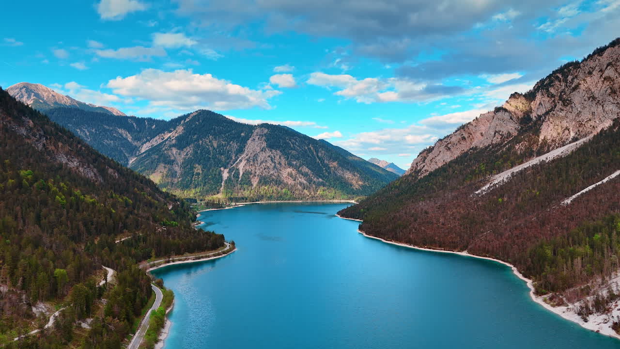 Flying above the peaceful azure lake Plansee in Reutte District, Tyrol, Austria. Drone footage among the stunning mountains covered with pine trees.